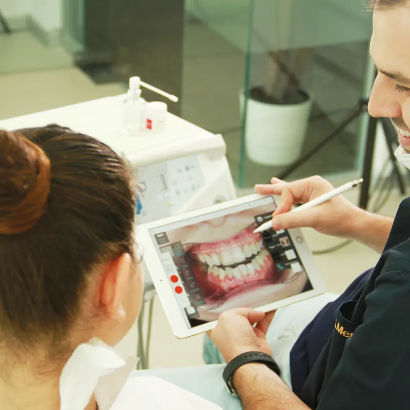 DENTAGLOBAL dentist reviewing photos with a patient on a tablet during a consultation
